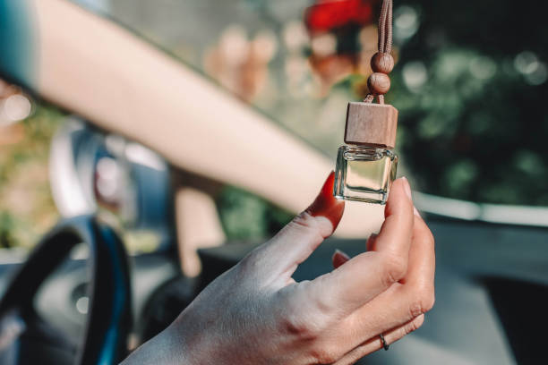 botella pequeña de vidrio con perfume de coche en mano femenina. pequeña botella de vidrio con perfume de coche colgando en el coche. - air freshener fotografías e imágenes de stock