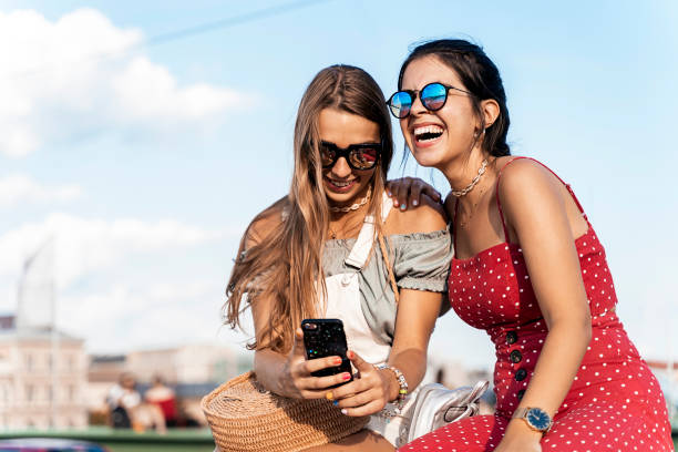 istock Happy female friends sitting on bridge and using smartphone 1171659520