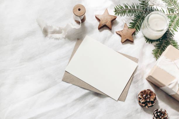 istock Christmas composition. Blank greeting card, envelope mock-up scene. Decorative corner. Pine cones, fir tree branches, gift box and wooden stars on white table, linen background. Flat lay, top view. 1171660808