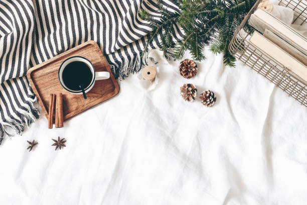 Christmas styled composition. Cup of coffee, plaid, old books in golden basket, pine cones, fir branches on white table, linen background. Flat lay, top view, winter holiday lifestyle concept, web banner. composición de estilo navideño. taza de café, a cuadros, libros viejos en cesta dorada, conos de pino, ramas de abeto sobre mesa blanca, fondo de lino. plano, vista superior. concepto de estilo de vida de vacaciones de invierno, banner web.