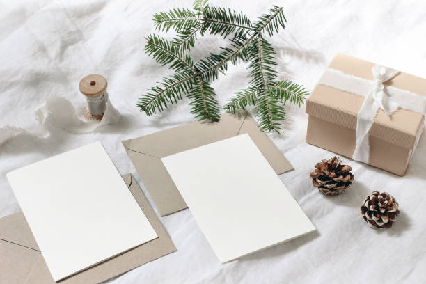 istock Christmas table, festive styled composition. Christmas greeting cards, envelopes mock-ups. Handmade gift box with silk ribbon, pine cones and fir tree branch on white linen background. Top view. 1171660829