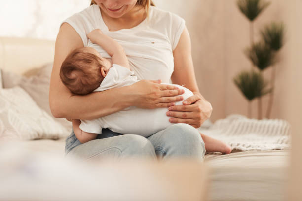 felice giovane madre godendo di nutrire il suo bambino appena nato con latte materno - domestic life family heterosexual couple young family foto e immagini stock