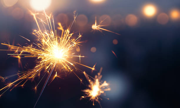 Glittering burning sparkler against blurred bokeh light background stock photo