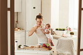 Morning of busy mother who is eating porridge for breakfast in kitchen while rocking her baby