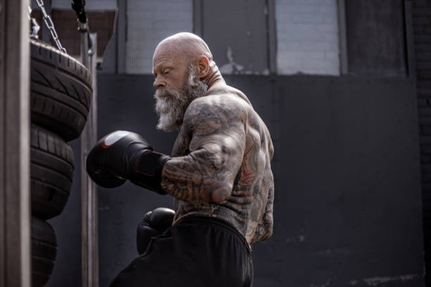 Tattooed Senior Boxer During Fighting Workout Bearded Aggressive Redhead Senior Man Boxer wearing gloves during outdoor workout old man boxing stock pictures, royalty-free photos & images
