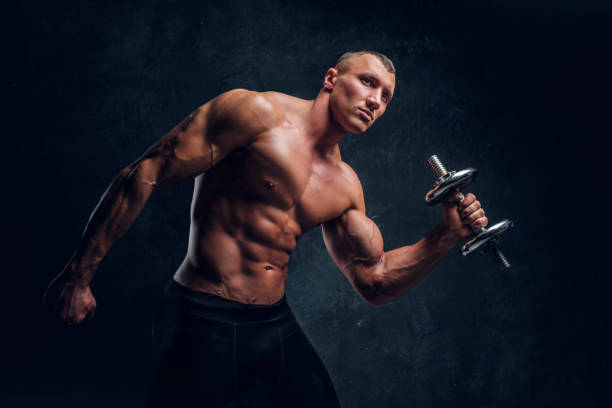 istock Young guy with a perfect pumped body posing with a dumbbell. Studio photo with dark wall background 1171674849