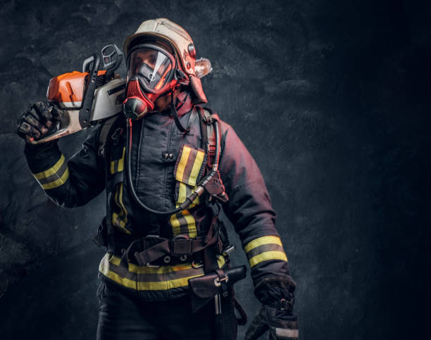 istock Firefighter wearing full protective equipment posing with a chainsaw on his shoulder. Studio photo against a dark textured wall 1171675052