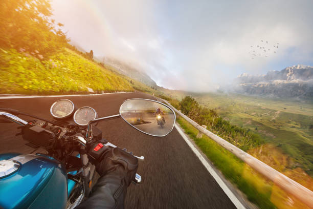 Motorcycle driver riding in Alpine highway, handlebars view, Dolomites, central Europe.