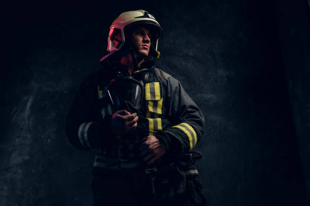 istock Brutal firefighter in uniform and safety helmet holding an oxygen mask and looking sideways with a confident look. 1171676364