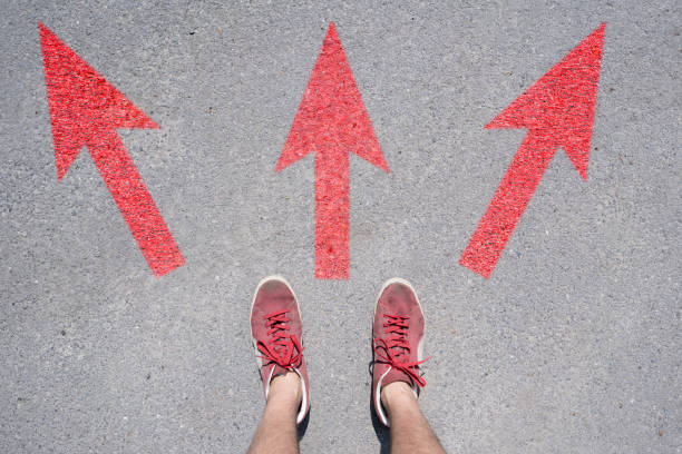 istock difficult to choose where to go, feet stand on the asphalt abstract surface with arrows 1171676530