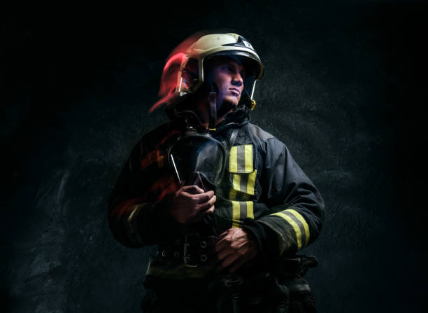 istock Brutal firefighter in uniform and safety helmet holding an oxygen mask and looking sideways with a confident look. 1171677500