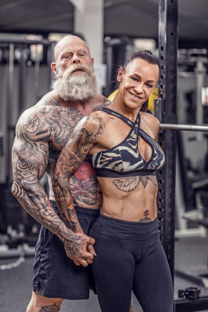 coppia senior tatuata durante l'allenamento in palestra - body building energy strength power foto e immagini stock