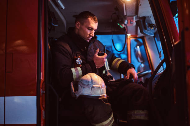 The fire brigade arrived at the night-time. Fireman sitting in the fire truck and talking on the radio stock photo