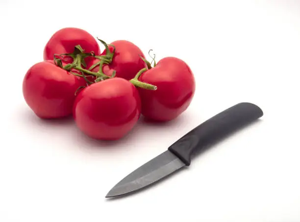 Five panicle tomatoes and a black ceramic knife isolated on white background. Selective focus.