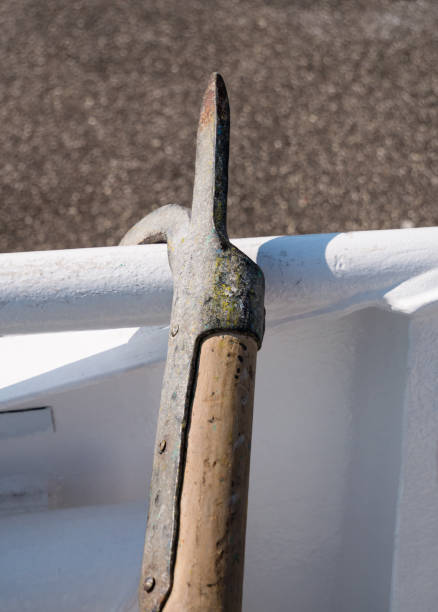 Close-up of old, used boothook made of metal and wood standing at white boat railing at mooring point at day.
