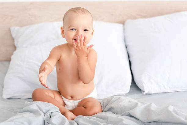 adorable barefoot child in diaper smiling while sitting on white bedding - one baby girl only fotos imagens e fotografias de stock