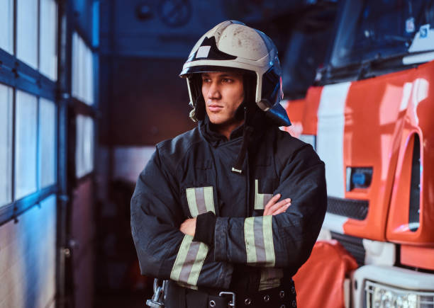 istock Fireman wearing protective uniform standing next to a fire engine in a garage of a fire department, crossed arms and looking sideways 1171680159