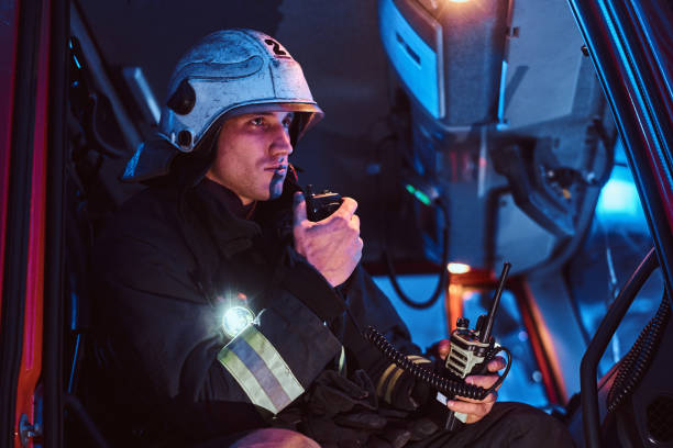 les pompiers sont arrivés à la nuit. pompier s'asseyant dans le camion de feu et parlant à la radio - walkie talkie photos et images de collection