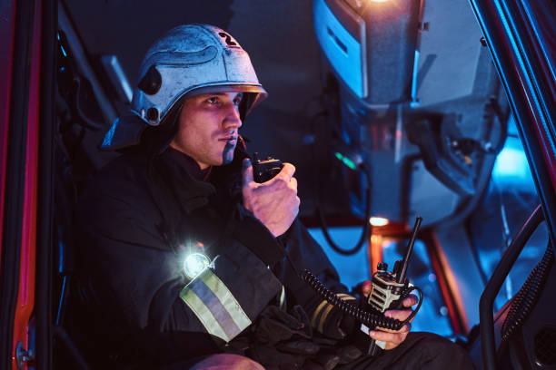 The fire brigade arrived at the night-time. Fireman sitting in the fire truck and talking on the radio The fire brigade arrived at the night-time. Fireman in a protective uniform sitting in the fire truck and talking on the radio walkie talkie photos stock pictures, royalty-free photos & images