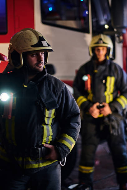 istock Two firemen wearing a protective uniform standing next to a fire truck. Arrival on call at night time 1171681275