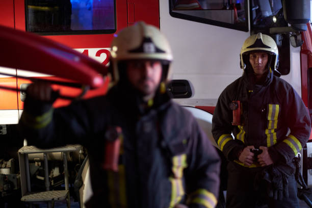 istock Two brave firemen wearing a protective uniform standing next to a fire truck. Arrival on call at night time 1171681489