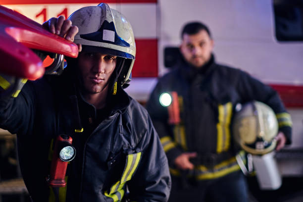 istock Two brave firemen wearing a protective uniform standing next to a fire truck. Arrival on call at night time 1171681575