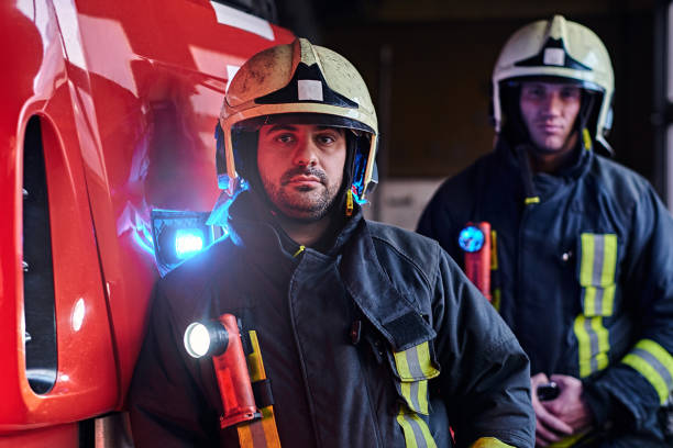 istock Two firemen wearing protective uniform standing next to a fire truck in a garage of a fire department. 1171682140