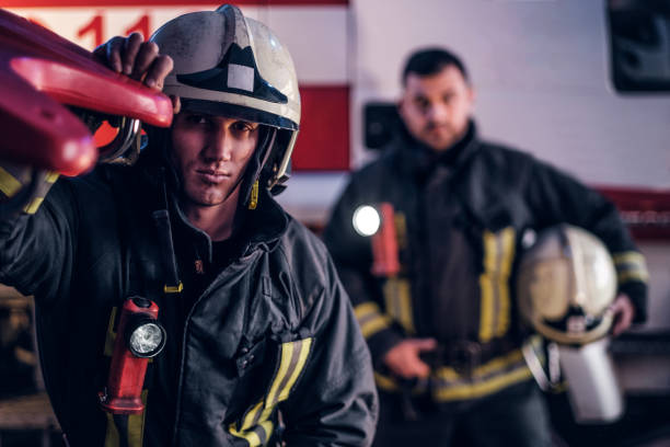 istock Two firemen wearing a protective uniform standing next to a fire truck. Arrival on call at night time 1171682183
