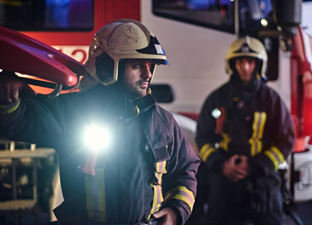 istock Two firemen wearing a protective uniform standing next to a fire truck. Arrival on call at night time 1171682303