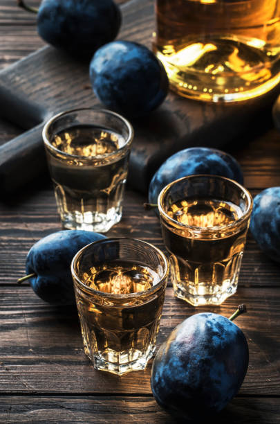 slivovica - brandy de ciruela o vodka de ciruela, licor duro, bebida fuerte en vasos sobre la mesa de madera vieja, ciruelas frescas, espacio de copia - slivovitz fotografías e imágenes de stock