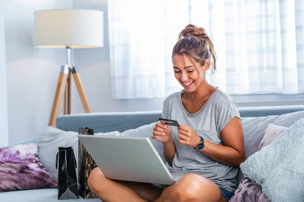 mujer joven sosteniendo tarjeta de crédito y usando computadora portátil. concepto de compras en línea. mujer feliz haciendo compras en línea en casa - women sofa teenage girls hairstyle fotografías e imágenes de stock