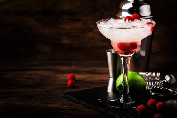 himbeer-daiquiri, alkoholischer cocktail mit weißem rum, limettensaft, himbeeren und zerkleinertem eis aus hohem glas, auf holzstangentheke mit stahlstangenwerkzeugen - crushed ice freshness red lime stock-fotos und bilder