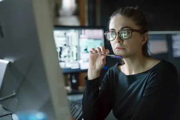 Stock photo of young woman’s face as she contemplates one of the many computer monitors that surround her.