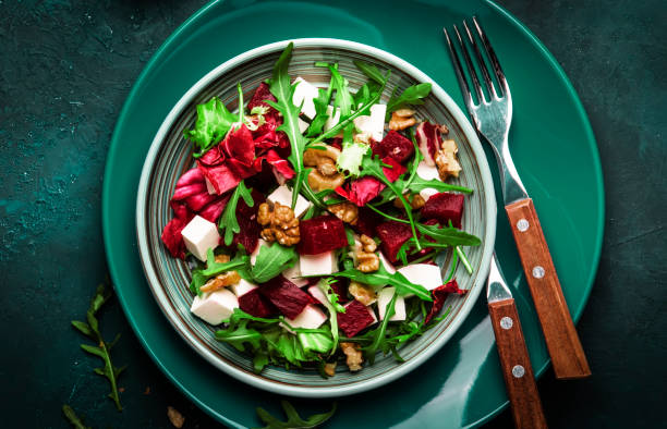 istock Arugula, Beet and cheese salad with fresh radicchio and walnuts on plate with fork, dressing and spices on blue kitchen table background, place for text, top view 1171688464