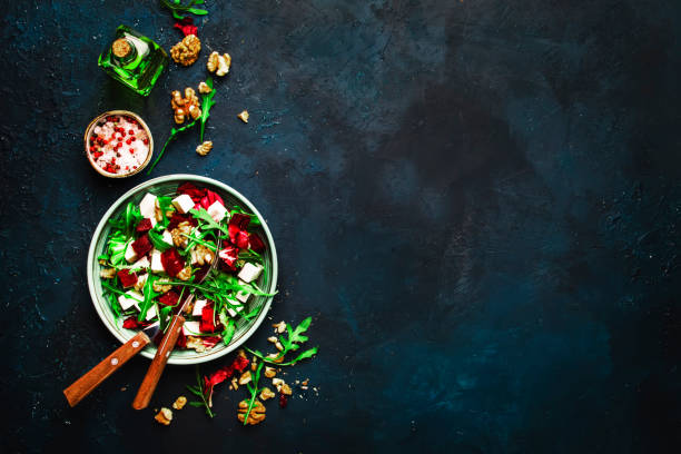 istock Arugula, Beet and cheese salad with fresh radicchio and walnuts on plate with fork, dressing and spices on blue kitchen table background, place for text, top view 1171688484