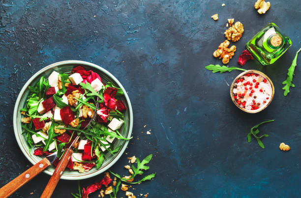 istock Arugula, Beet and cheese salad with fresh radicchio and walnuts on plate with fork, dressing and spices on blue kitchen table background, place for text, top view 1171688500