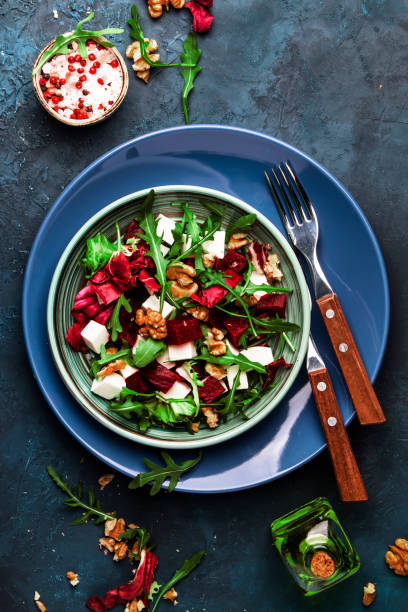 istock Arugula, Beet and cheese salad with fresh radicchio and walnuts on plate with fork, dressing and spices on blue kitchen table background, place for text, top view 1171688522