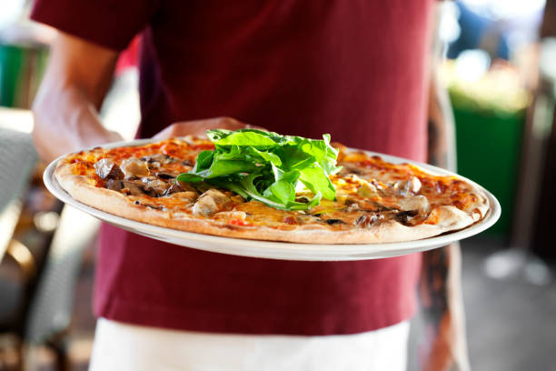 Photo of waiter at a restaurant serving pizza