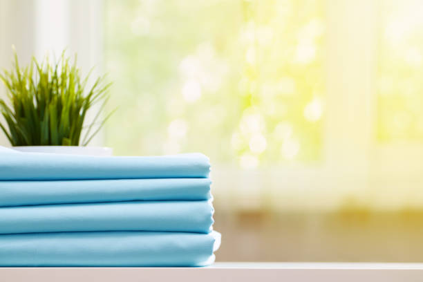 istock Closeup of blue clean bedding on a blurred background. A stack of folded new bed sheets on the table. Sunlight from the window 1171689380