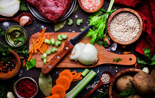 Food cooking background. Fresh organic vegetables, ingredients, spices and meat for warm autumn soup on vintage kitchen table with rustic wooden cutting board. Top view, place for text. Domestic cooking and eating concept