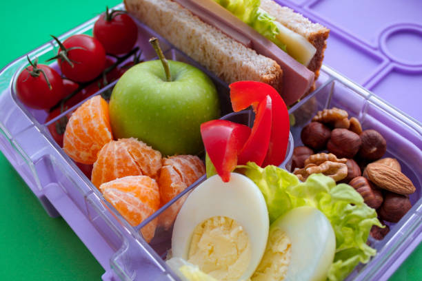 fermez-vous vers le haut de la boîte à lunch de lilac avec la nourriture utile pour le déjeuner et la casse-croûte : sandwich, légumes, fruits, noix sur un fond vert clair. concept d'aliments sains, collation pour adultes et enfants - lunch box lunch red apple photos et images de collection
