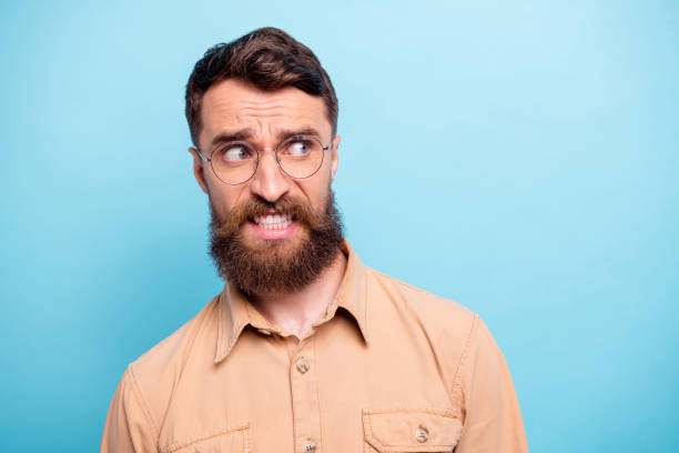 foto de cerca de tipo frustrado mirando usando gafas camisa marrón aislado sobre fondo azul - frustration terrified worried glasses fotografías e imágenes de stock