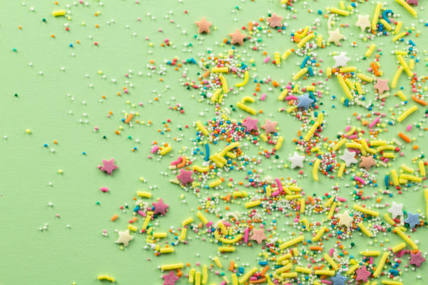 istock Sprinkles on pale green background - Assorted colourful cake topping sprinkles sprayed on green on bottom corner with space for text - top view of star shapes, dots and oblong sprinkles 1171714649