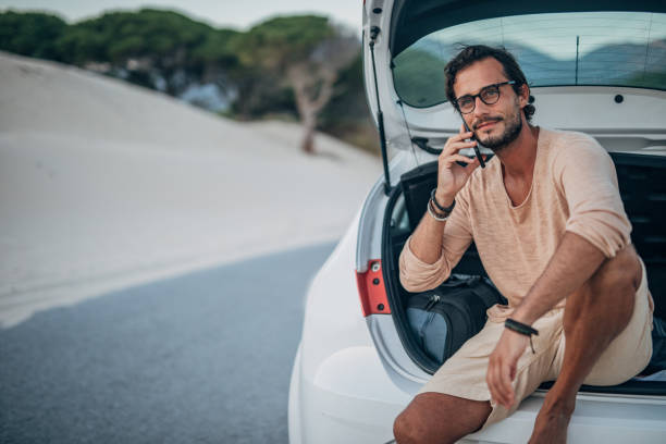 istock Guy sitting on car trunk and talking on phone 1171722190