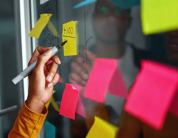 Photo of Close-up of businesswoman writing on yellow sticky notes stuck o