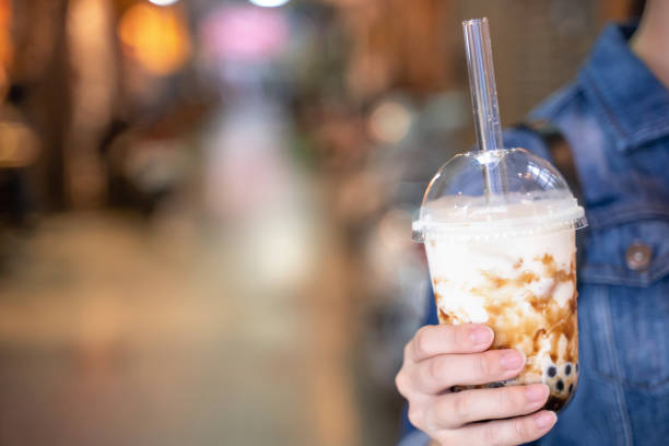 istock Young girl in denim jacket is drinking brown sugar flavored tapioca pearl bubble milk tea with glass straw in night market of Taiwan. 1171723725