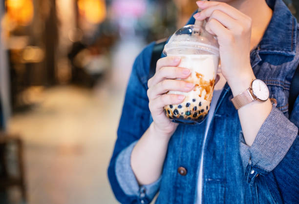 istock Young girl in denim jacket is drinking brown sugar flavored tapioca pearl bubble milk tea with glass straw in night market of Taiwan. 1171723726