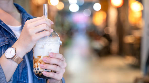 istock Young girl in denim jacket is drinking brown sugar flavored tapioca pearl bubble milk tea with glass straw in night market of Taiwan. 1171723730