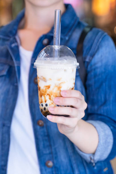 istock Young girl in denim jacket is drinking brown sugar flavored tapioca pearl bubble milk tea with glass straw in night market of Taiwan. 1171723745