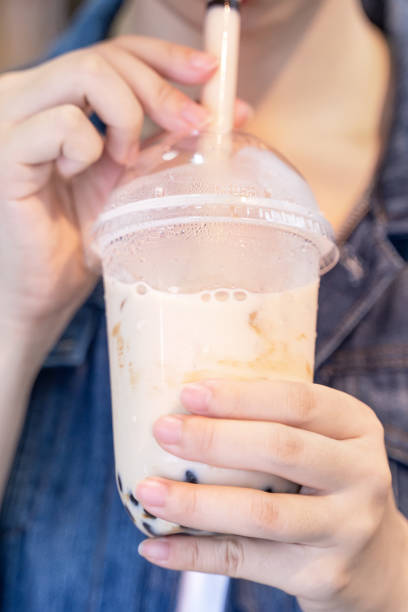istock Young girl in denim jacket is drinking brown sugar flavored tapioca pearl bubble milk tea with glass straw in night market of Taiwan. 1171723757